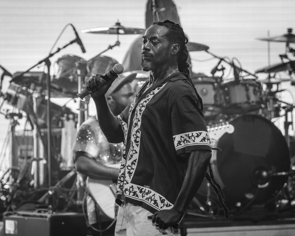 Buju-Banton-Roots-and-Reggae-Concert-Pacific-Amphitheatre-OC-June-19-2026-2026888 – The 824 Journal Male vocalist with braided hair singing into a microphone on stage during a live performance, drums in the background.