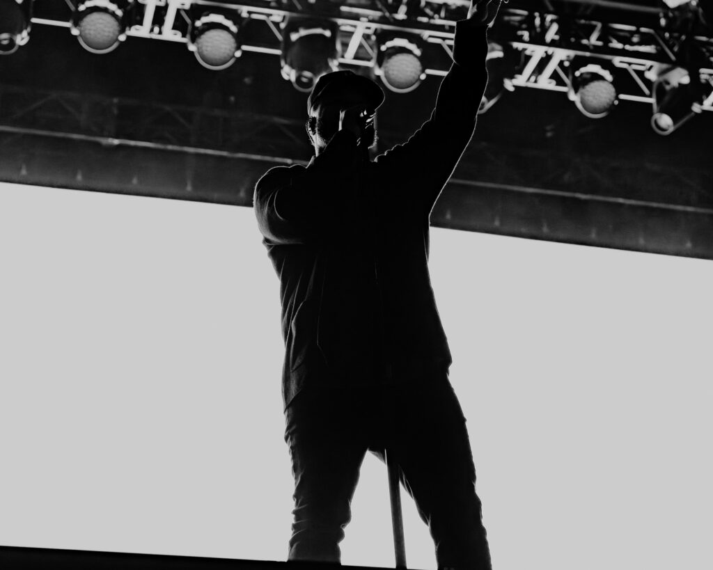 Common-Kings-Concert-Los-Angeles-May-23-2026-by-Zharmaaaine-45 – The 824 Journal Silhouette of a singer on stage, holding a microphone and raising one arm against bright stage lights (black and white).