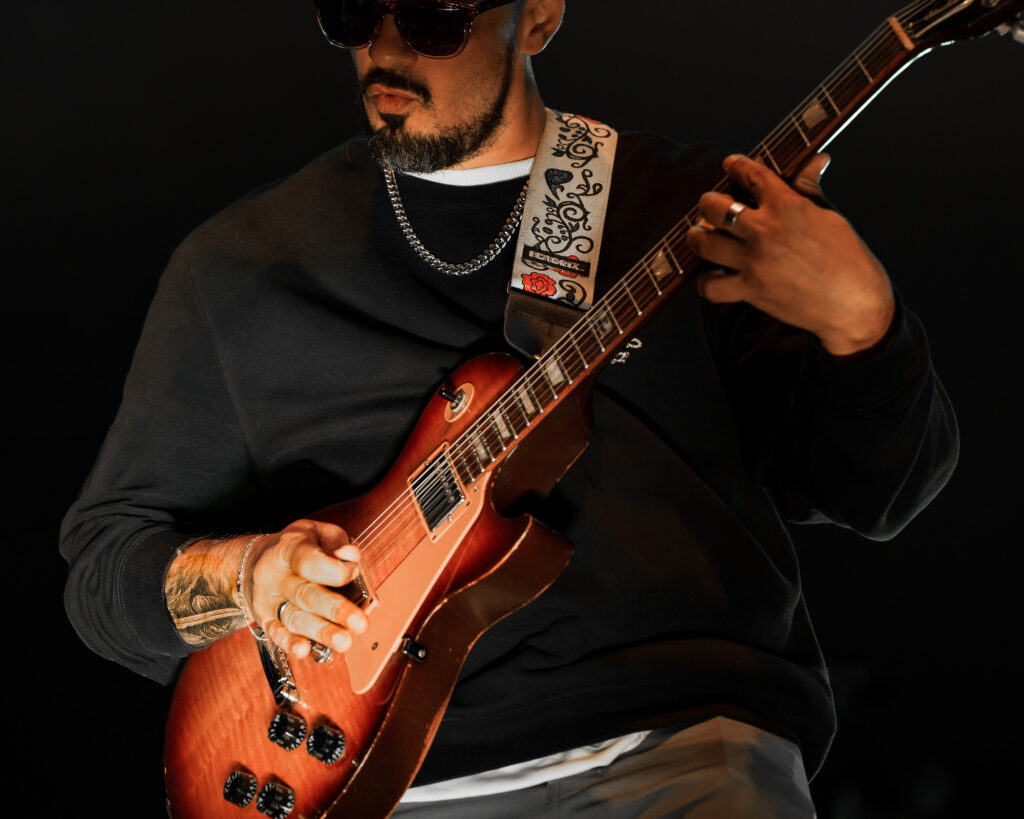 Common-Kings-Concert-Los-Angeles-May-23-2026-by-Zharmaaaine-79 – The 824 Journal Guitarist wearing sunglasses plays a sunburst electric guitar, close-up of hands on the fretboard with a patterned strap and silver chain necklace.