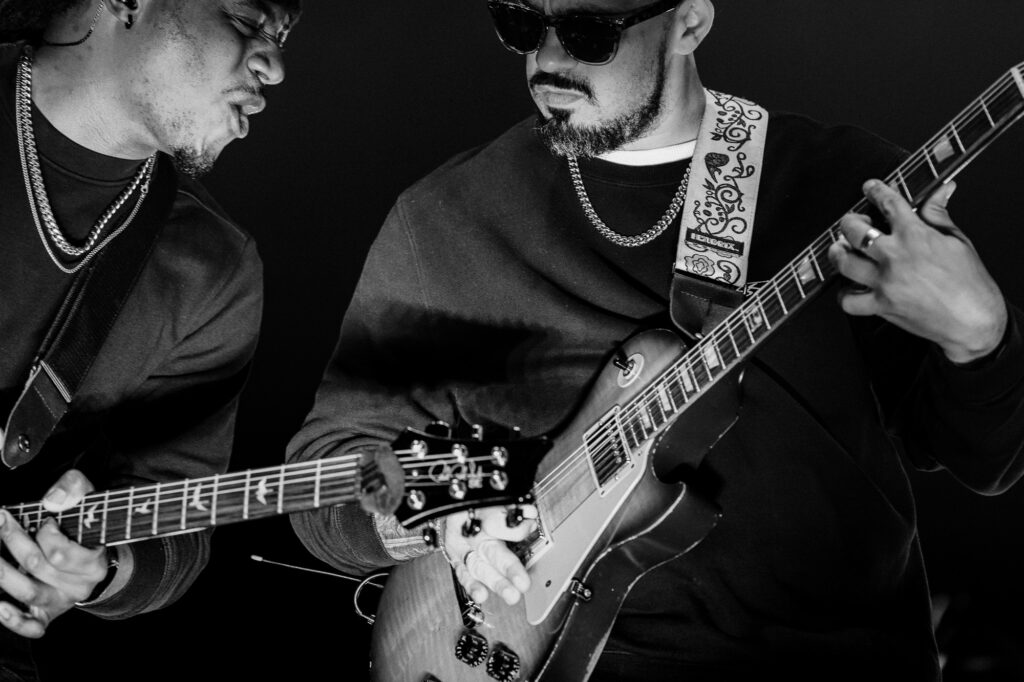 Common-Kings-Concert-Los-Angeles-May-23-2026-by-Zharmaaaine-80 – The 824 Journal Two male guitarists playing electric guitars in a black-and-white photo, one wearing sunglasses and a decorative strap.