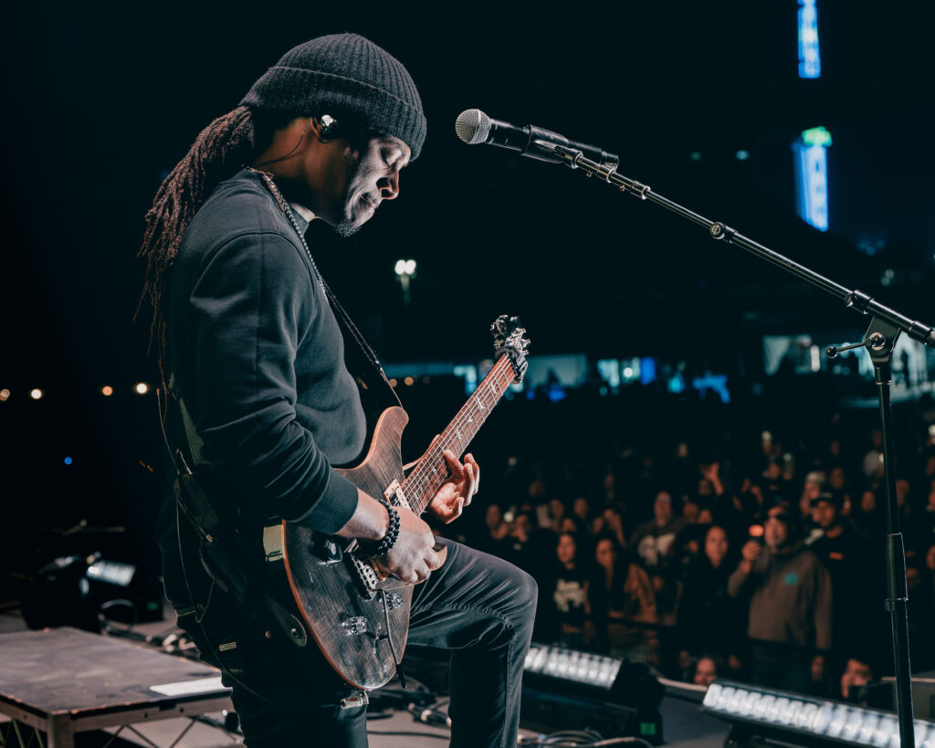 Common-Kings-Concert-Los-Angeles-May-23-2026-by-Zharmaaaine-97 – The 824 Journal Guitarist on stage wearing a black beanie, playing an electric guitar into a microphone with a blurred crowd in the background.
