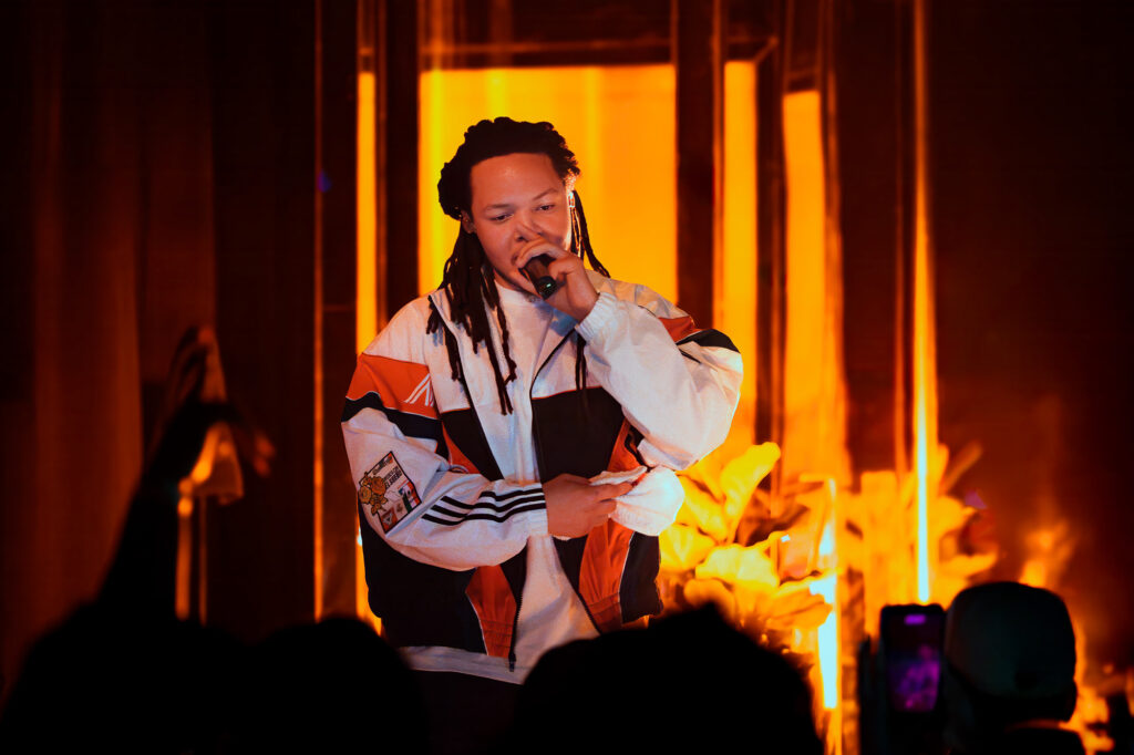 Domani-The-Echo-Los-Angeles-June-23-2026-by-Zharmaine-Boatman-IG-zharmaaaine-13-2 – The 824 Journal Singer performing on stage with a microphone, bathed in warm orange lights, wearing a color-block jacket; audience silhouettes in foreground.