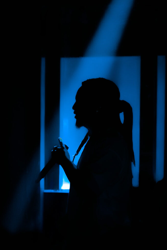 Domani-The-Echo-Los-Angeles-June-23-2026-by-Zharmaine-Boatman-IG-zharmaaaine-17-2 – The 824 Journal Silhouette of a person in profile with a ponytail, holding a microphone against blue stage lighting.