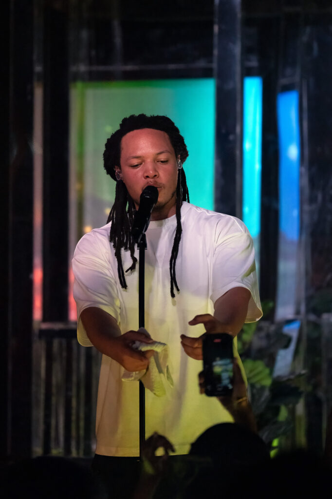 Domani-The-Echo-Los-Angeles-June-23-2026-by-Zharmaine-Boatman-IG-zharmaaaine-18-2 – The 824 Journal Male singer with dreadlocks performing into a microphone on a dim stage with colorful backlights behind him.