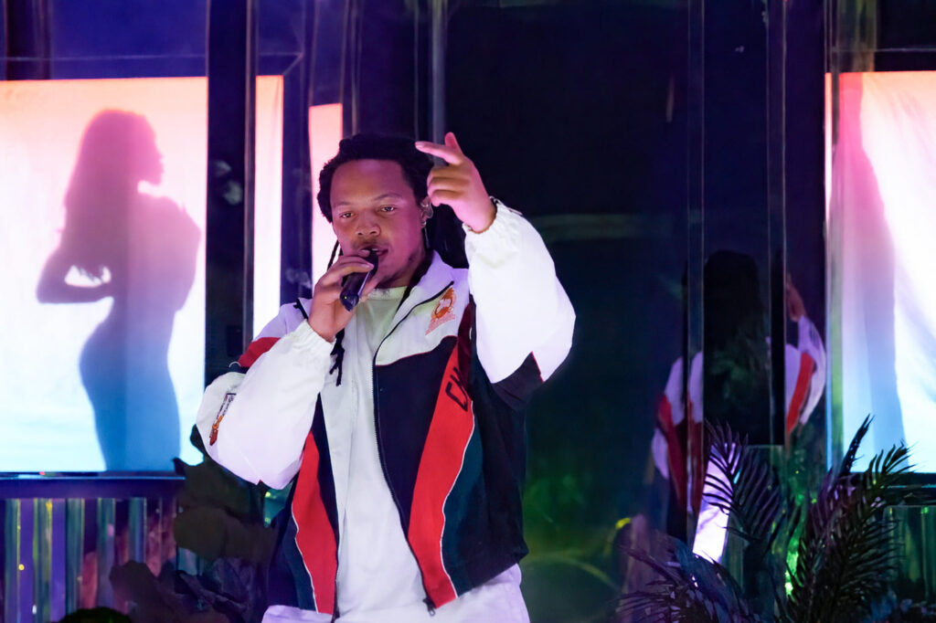 Domani-The-Echo-Los-Angeles-June-23-2026-by-Zharmaine-Boatman-IG-zharmaaaine-25 – The 824 Journal Male performer singing into a handheld microphone on a colorful stage with neon-lit panels behind him and his reflection visible in mirrored surfaces.