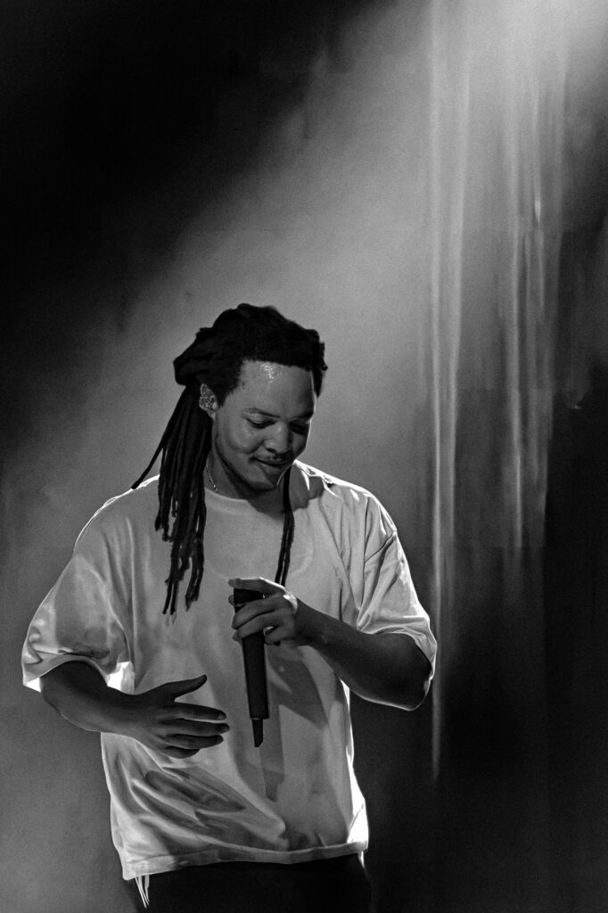 Domani-The-Echo-Los-Angeles-June-23-2026-by-Zharmaine-Boatman-IG-zharmaaaine-29 – The 824 Journal Black-and-white photo of a man with long dreadlocks in a white shirt on stage, holding a microphone and looking down as he performs.