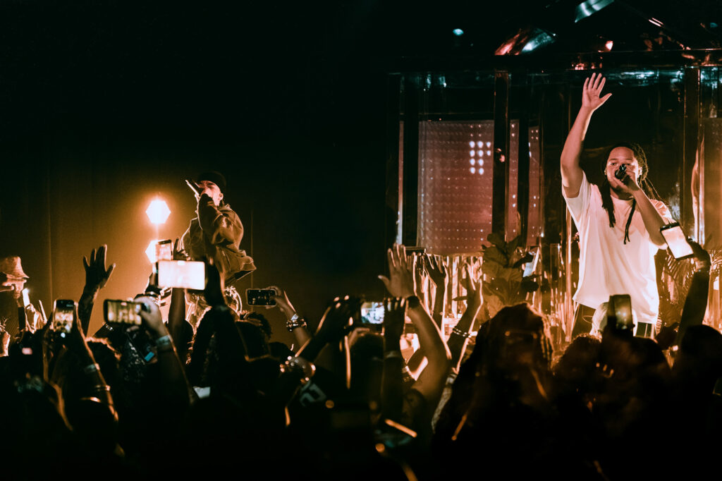 Domani-The-Echo-Los-Angeles-June-23-2026-by-Zharmaine-Boatman-IG-zharmaaaine-32-2 – The 824 Journal Two performers on a dark stage surrounded by a cheering crowd, fans raise phones to capture the moment as bright orange lights glow behind them.
