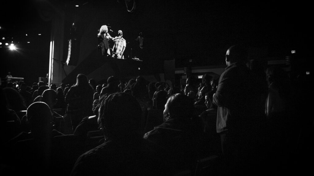 Musiq-Soulchild-The-Grove-of-Anaheim-May-29-2026-40 – The 824 Journal Dark concert venue with a crowd watching a stage performance shown on a large screen above the audience from behind.