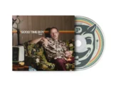 Man relaxing on a floral sofa in a retro room, holding a drink, with a large vinyl record edge showing on the right.