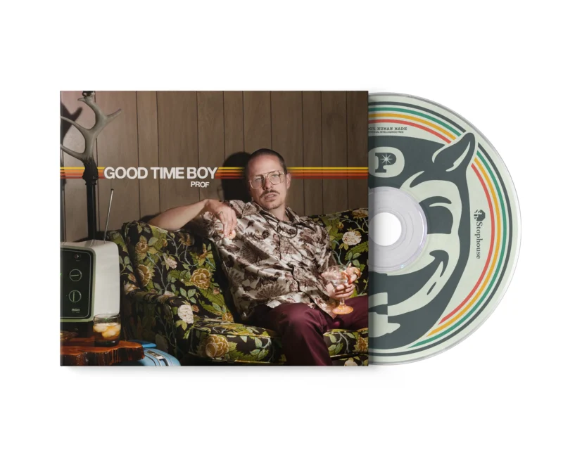 Man relaxing on a floral sofa in a retro room, holding a drink, with a large vinyl record edge showing on the right.