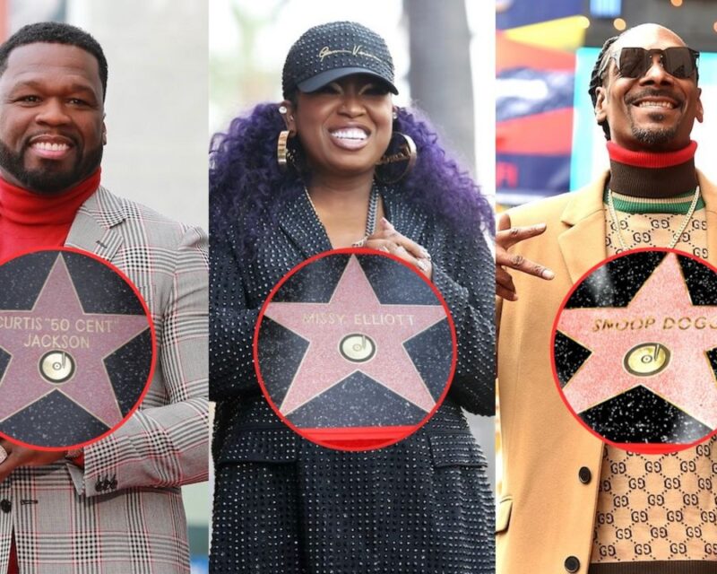 Three smiling adults pose with pink star plaques encircled in red, standing on a city street; left wears a gray plaid suit, middle in black dotted outfit, right in tan coat and sunglasses.