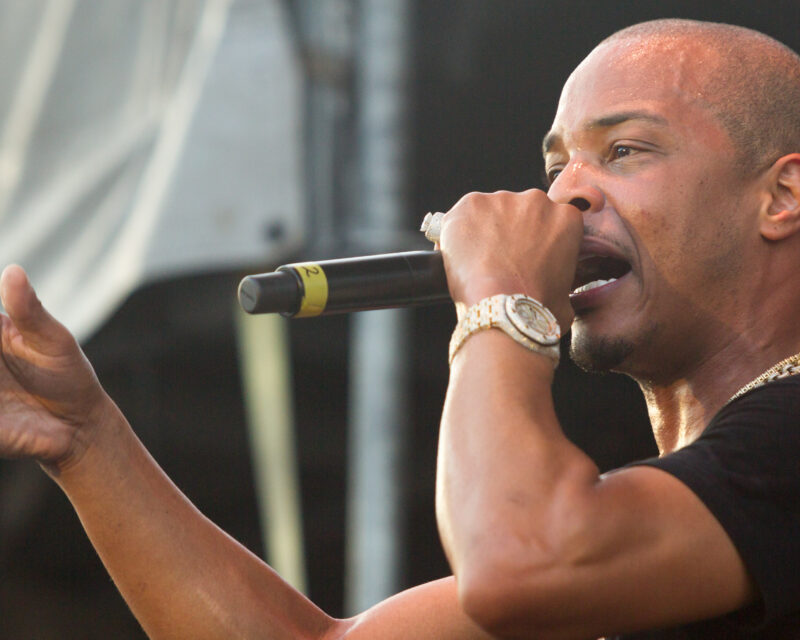 Male singer on stage, singing into a microphone with his left hand extended toward the audience.