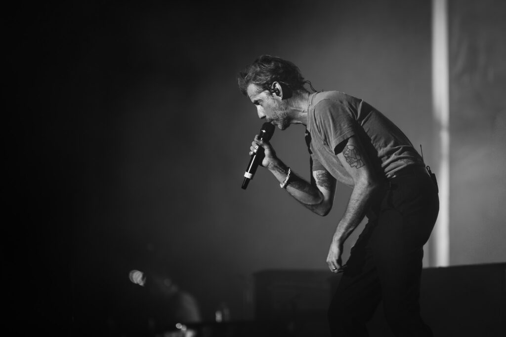 Male singer performs on stage, close-up profile with microphone and in-ear monitor in his ear, black-and-white image.