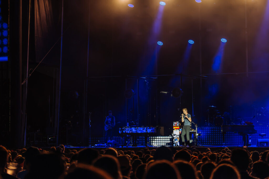 Pop singer on stage under blue and purple spotlights, performing to a crowded audience.