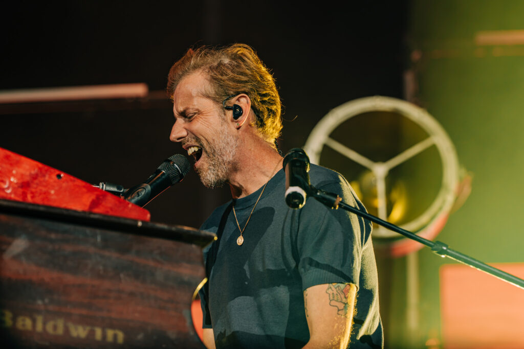 Male singer at a keyboard, passionately singing into a microphone with in-ear monitors on stage