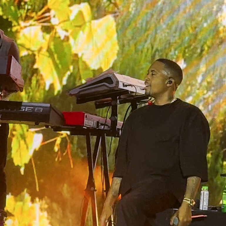 Screenshot – The 824 Journal Smiling man in a black shirt sits on stage beside a keyboard and synth setup during a performance.