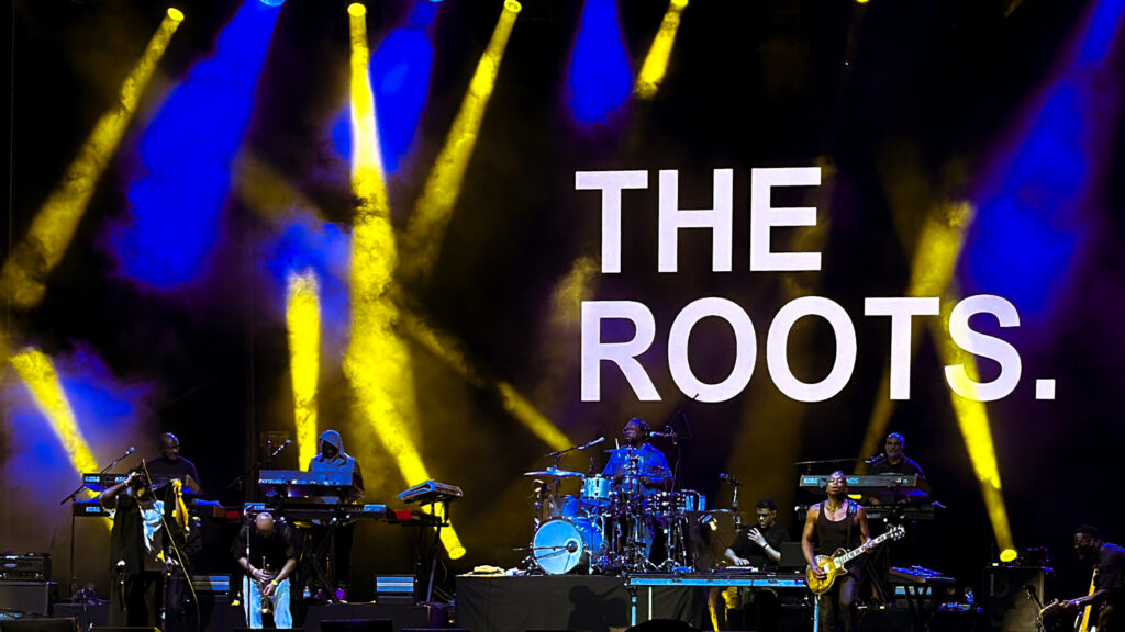 Nas-The-Roots-De-La-Soul-Great-Night-in-Hip Hop-08 – The 824 Journal Concert stage performance by The Roots with yellow and blue lighting and the band performing on stage under a large screen displaying 'THE ROOTS'