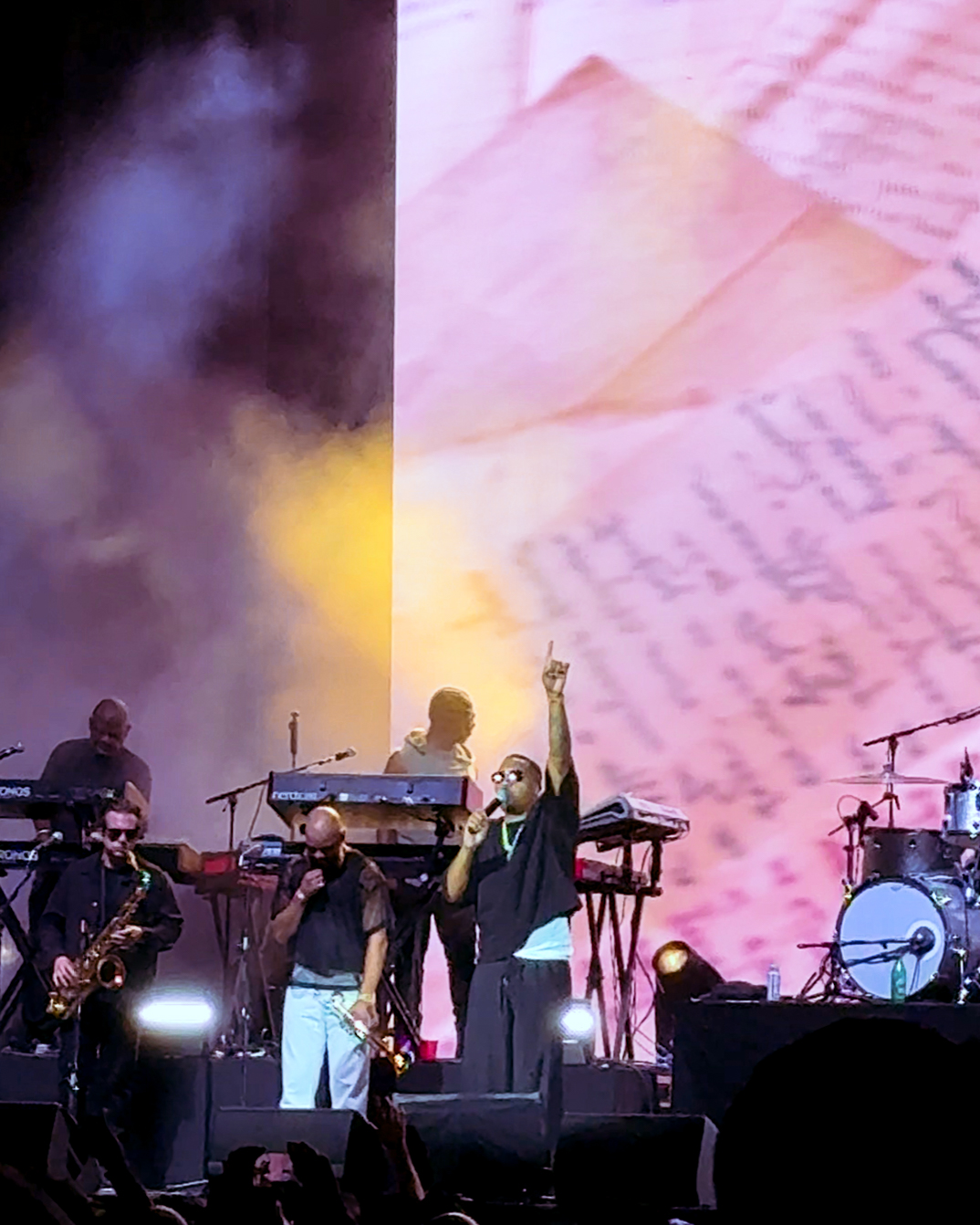 Screenshot – The 824 Journal Band performs on a smoky stage; the lead singer raises a hand while backup musicians play keyboards and saxophone, pink light backdrop overall.
