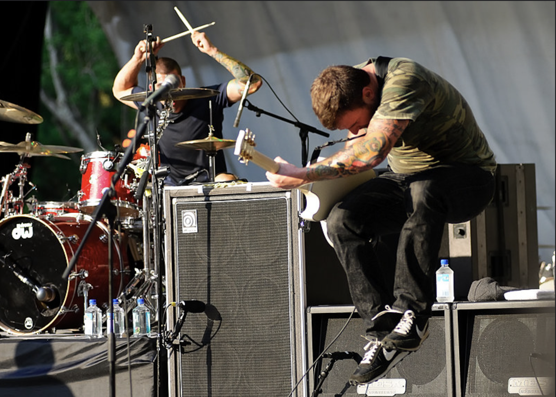 New Found Glory guitarist Chad Gilbert performing on stage beside the drum kit.