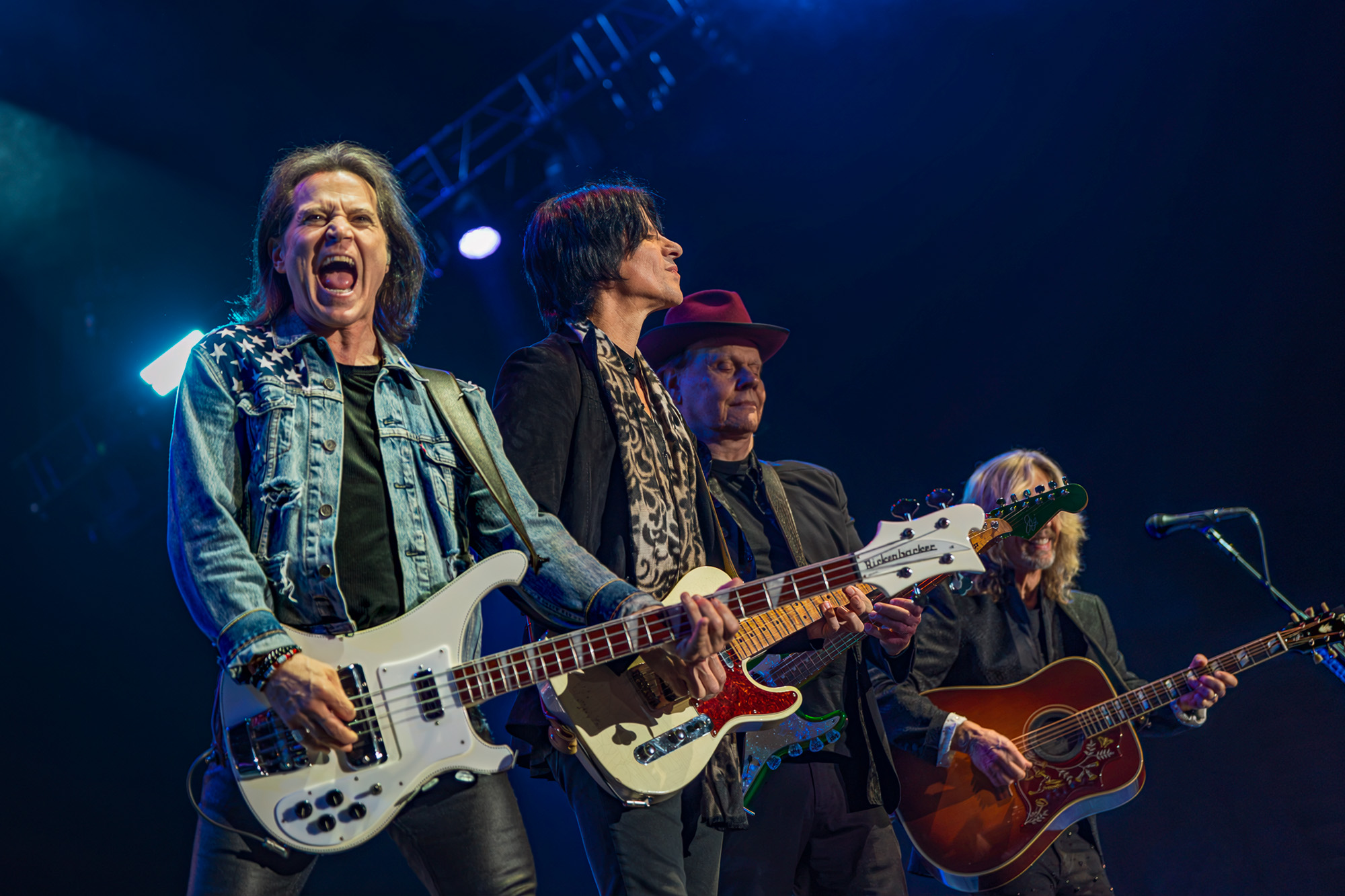 Styx at The Kia Forum in Inglewood: a rock band performing on stage with multiple guitarists under blue stage lights.