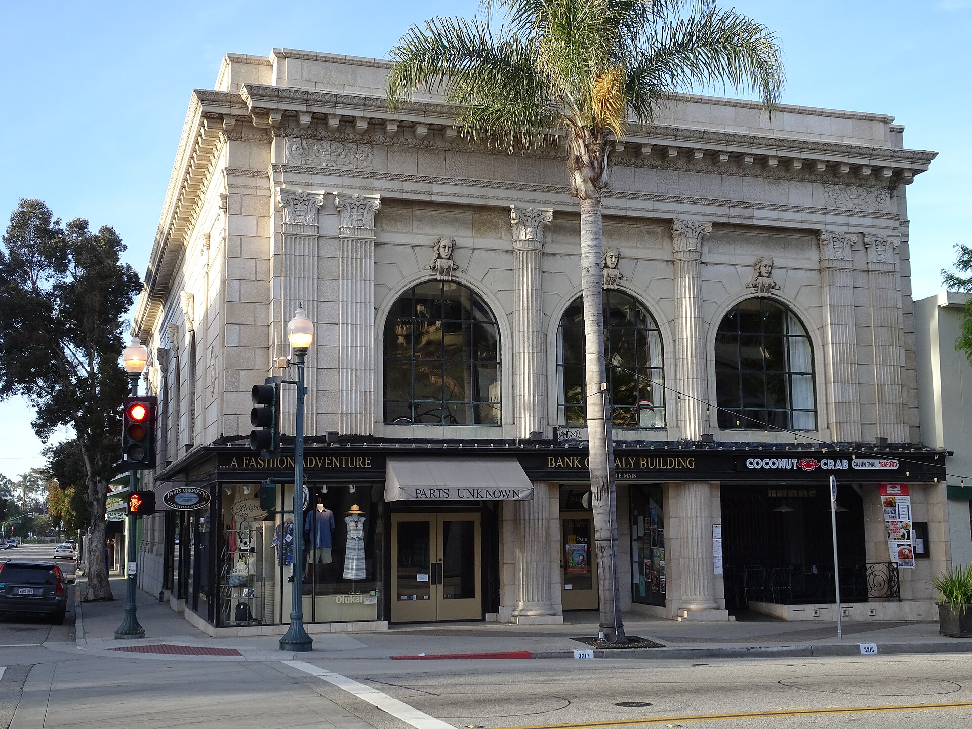 The white neoclassical Bank of Italy building with tall arched windows on the corner of East Main Street in downtown Ventura, with a palm tree beside it