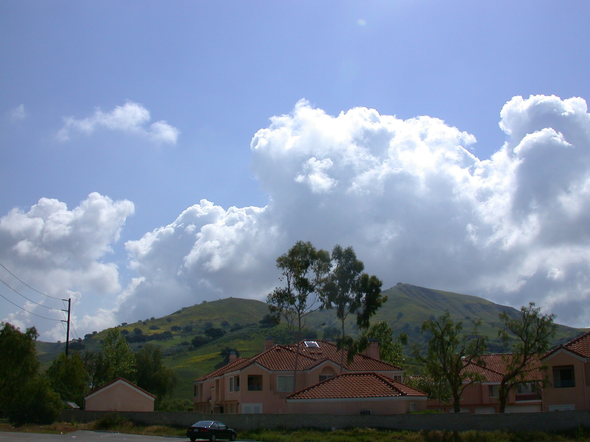 Red-roofed homes below green hills and big white clouds near Lost Hills Road in Calabasas