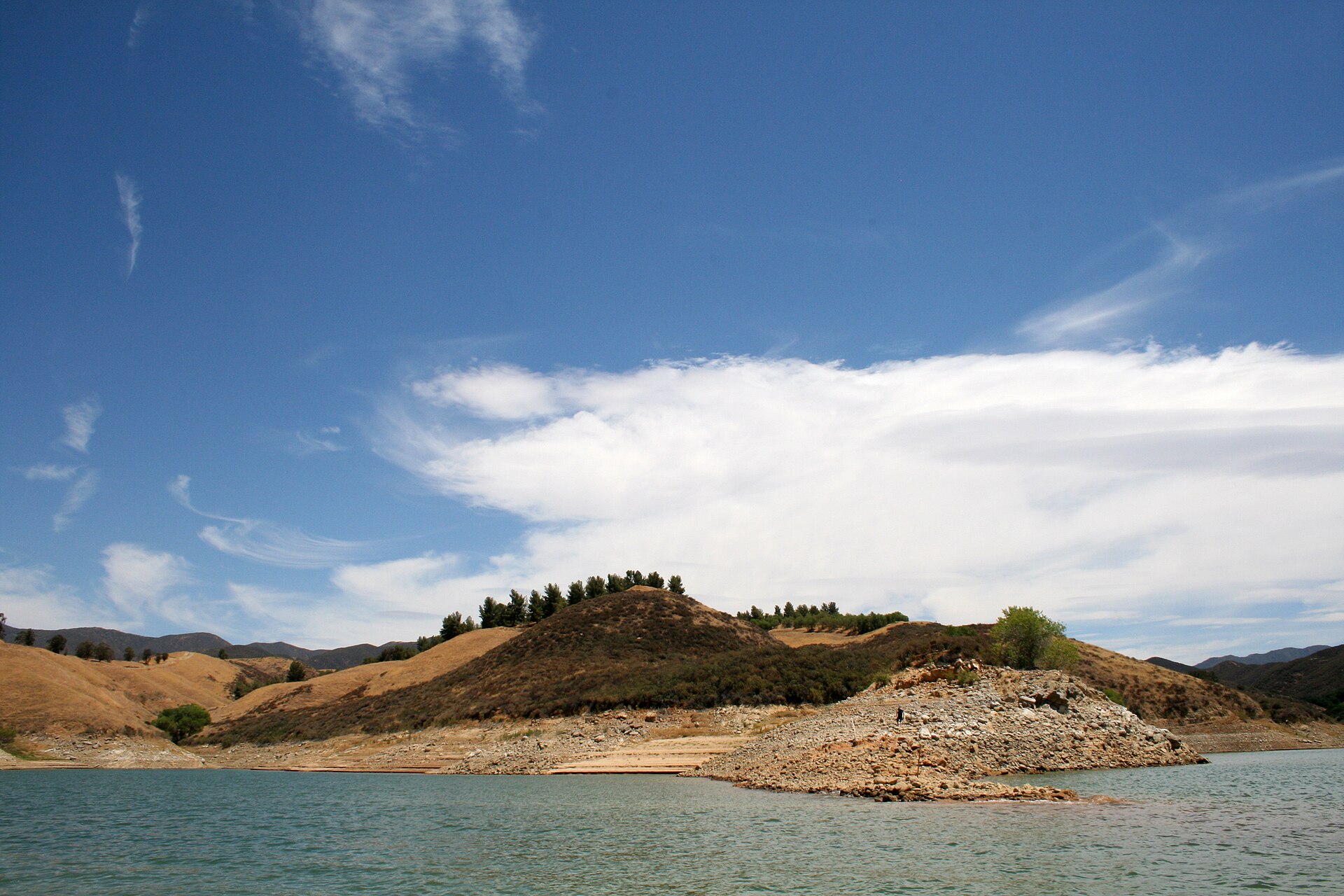 Castaic Lake surrounded by dry golden hills under a blue sky with scattered clouds