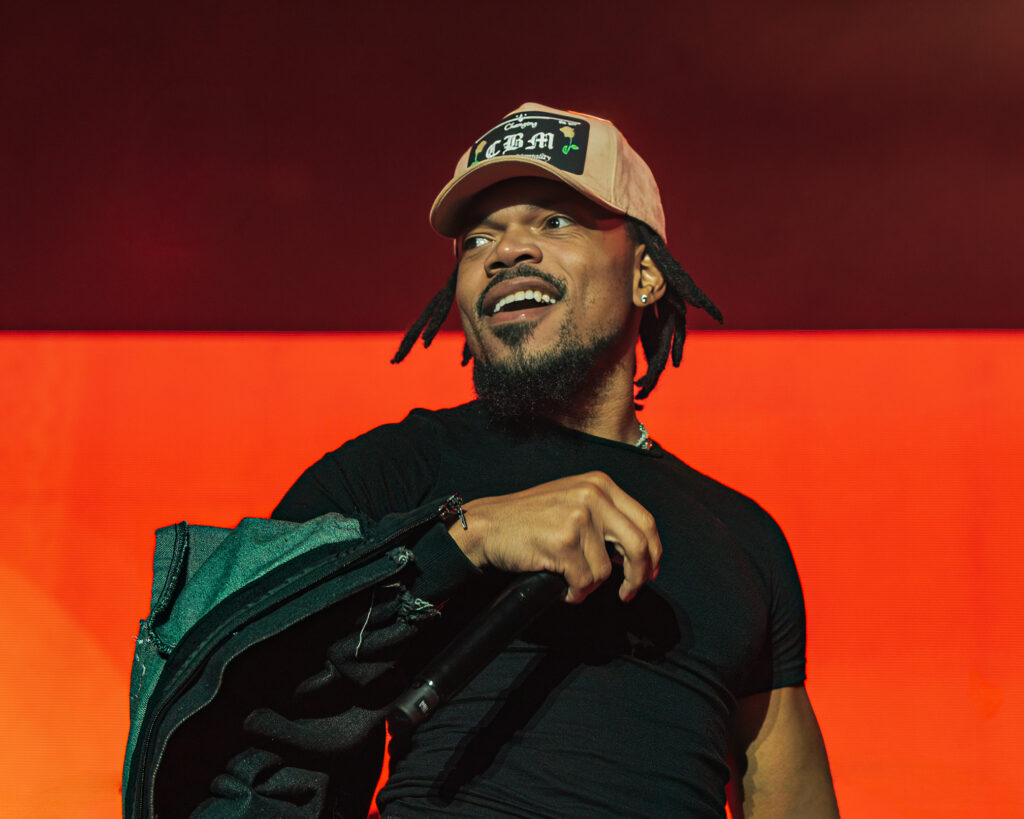 Chance the Rapper at Hollywood Palladium, Los Angeles, September 20, 2026 (6) – The 824 Journal Chance the Rapper smiling with a denim jacket over his arm against a red-orange backdrop at the Hollywood Palladium.