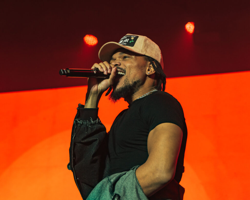 Chance the Rapper at Hollywood Palladium, Los Angeles, September 20, 2026 (7) – The 824 Journal Chance the Rapper singing into a microphone, jacket in hand, against a bright orange backdrop at the Hollywood Palladium.