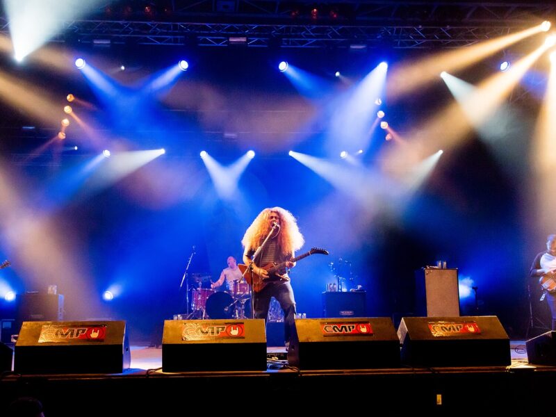 Coheed and Cambria performing on a large outdoor festival stage under bright white and blue stage lights