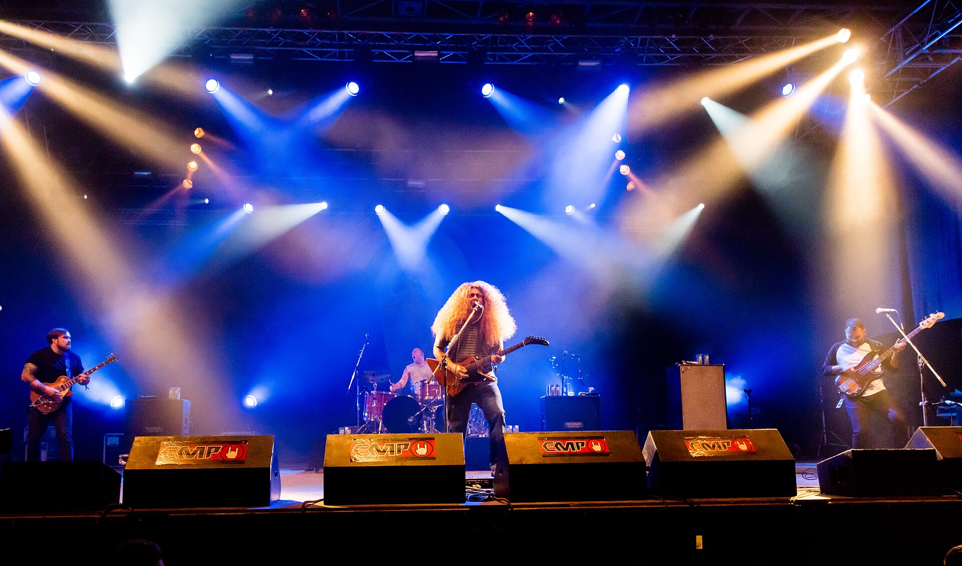 Coheed and Cambria performing on a large outdoor festival stage under bright white and blue stage lights