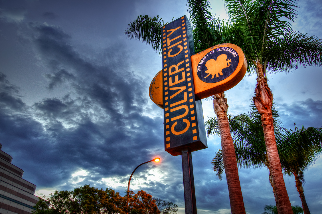 The vertical Culver City municipal sign between palm trees under a dramatic dusk sky