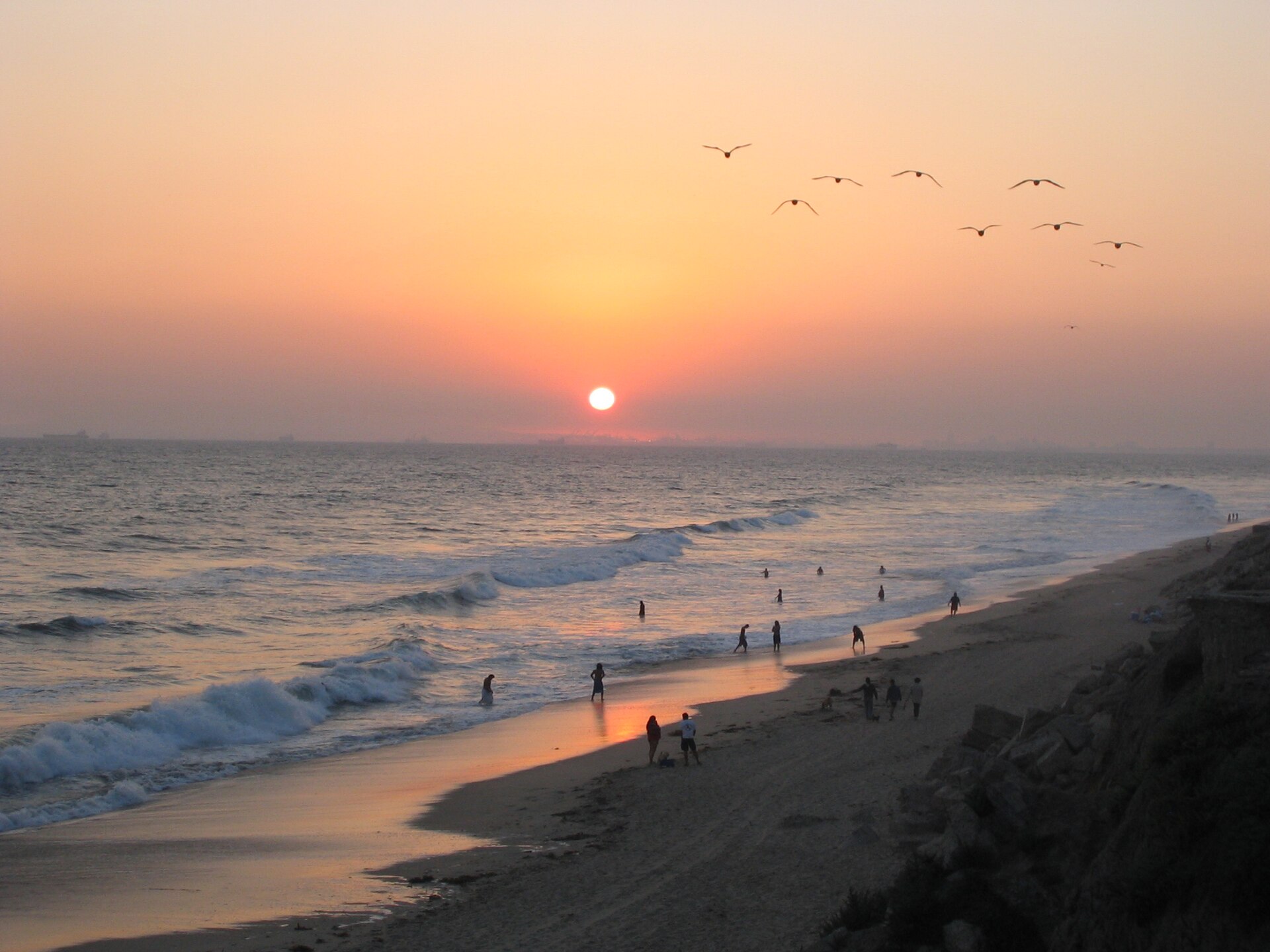 The sun setting over the Pacific Ocean at Huntington Beach, with waves rolling onto the sand