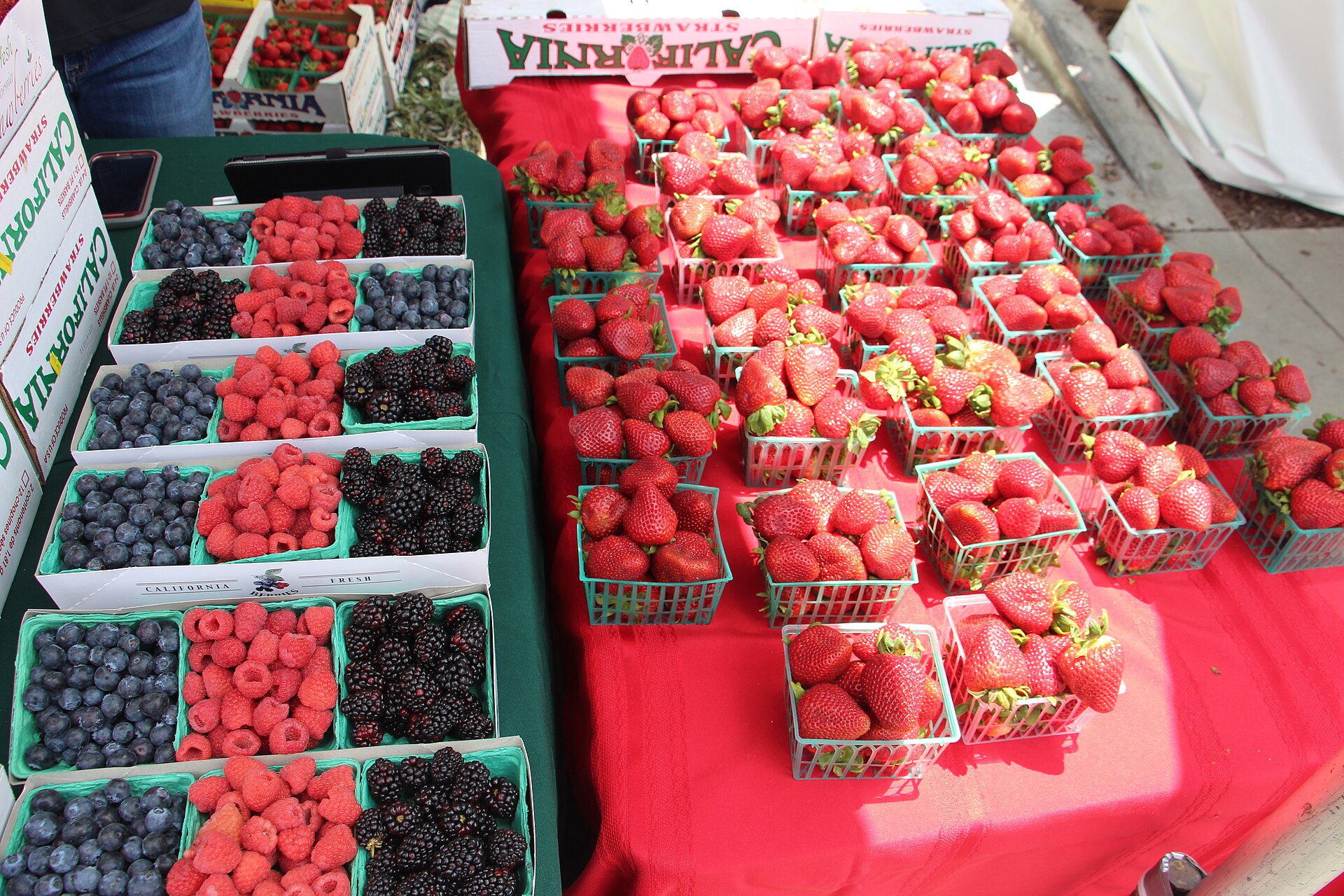 Baskets of strawberries, raspberries, blueberries, and blackberries stacked on a red-draped table at the Garden Grove Strawberry Festival