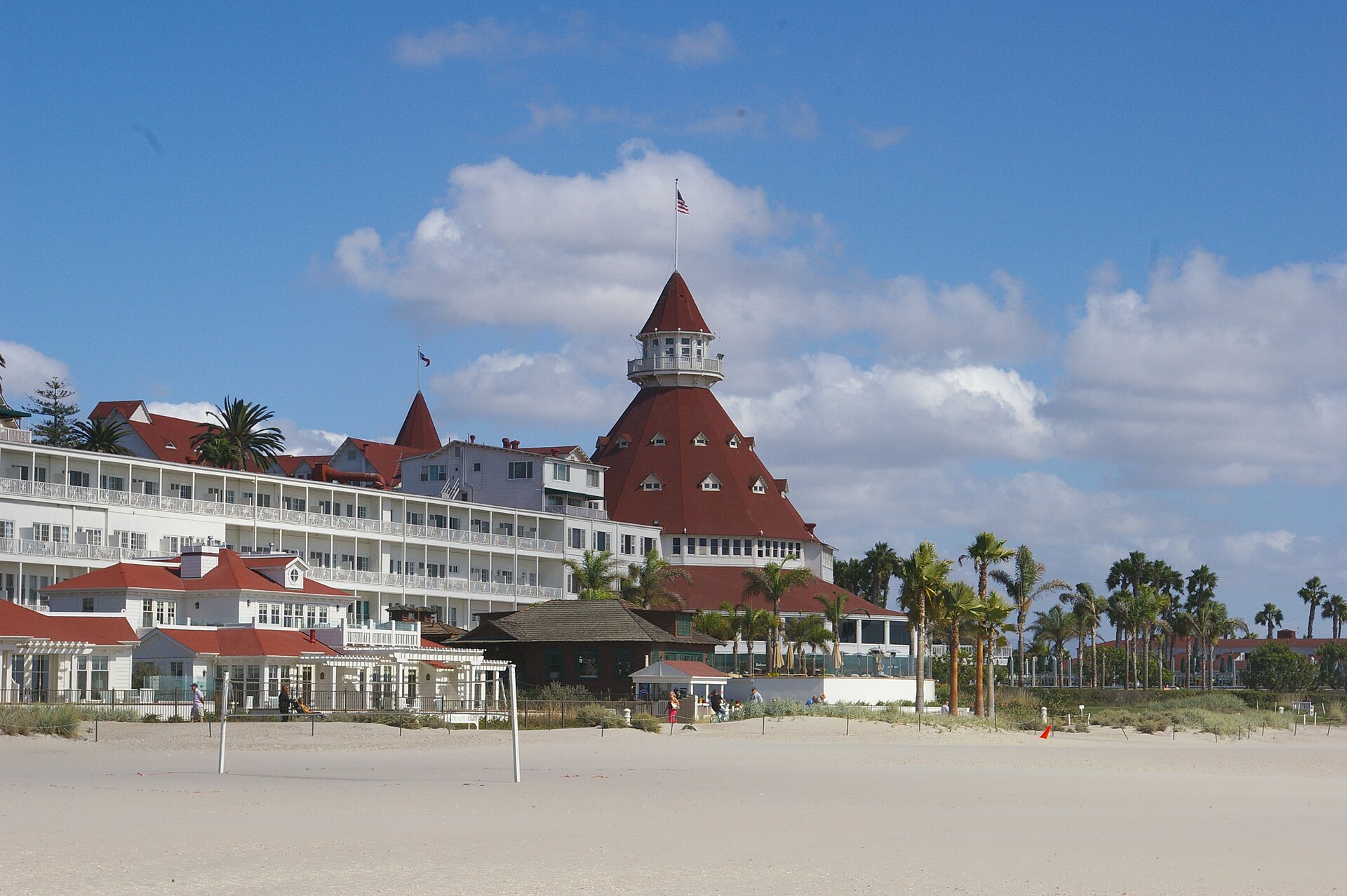 The white Victorian Hotel del Coronado with its red turret roof, seen from the sand under a blue sky with clouds