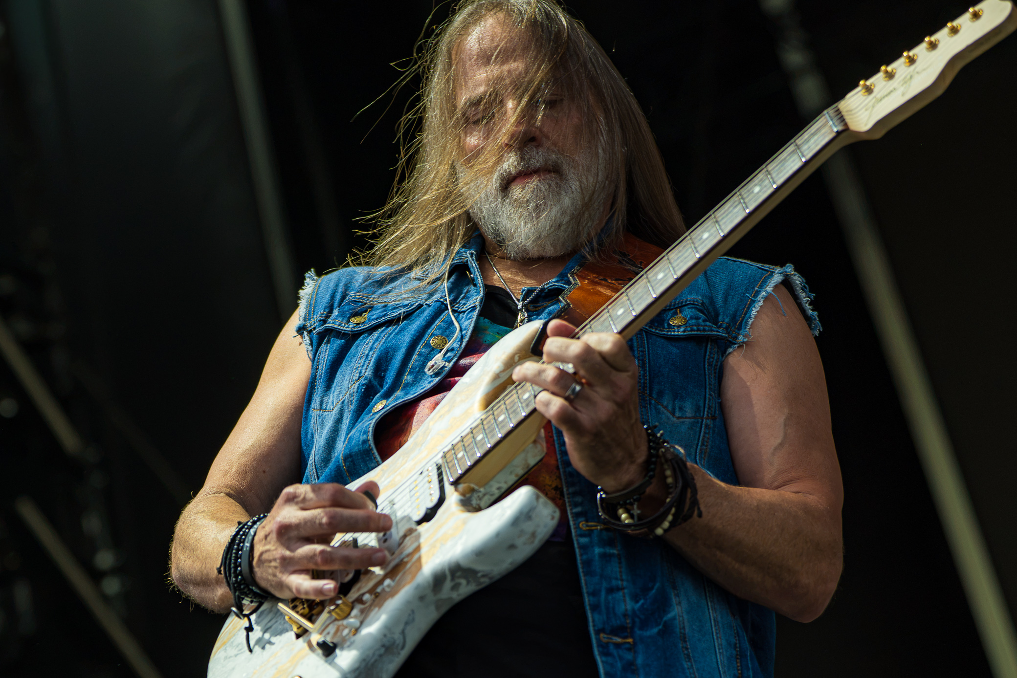 Kansas at F&M Bank Amphitheater in Long Beach: guitarist with long hair and a beard, wearing a denim vest, playing a white electric guitar on stage.