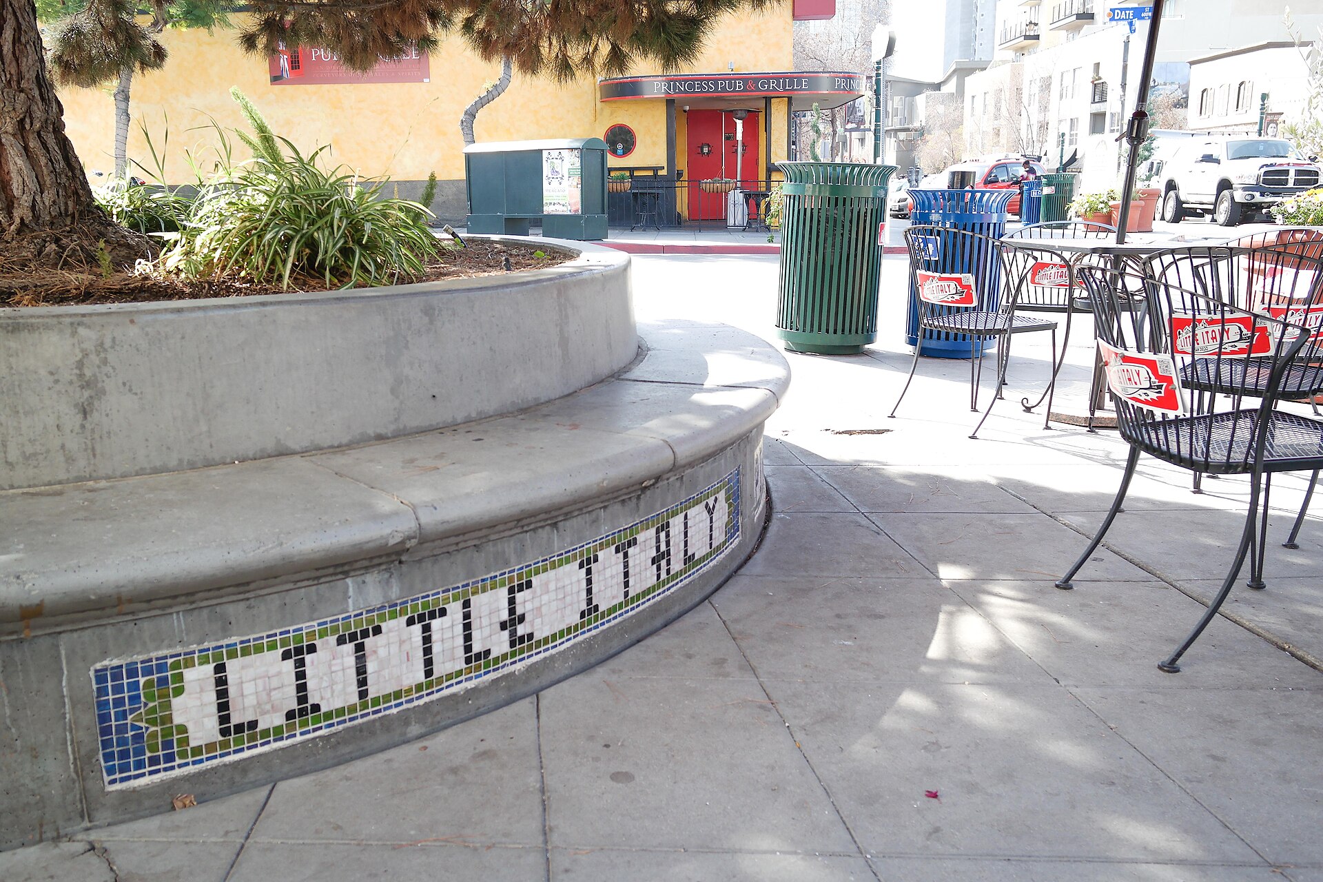 A curved planter with Little Italy spelled out in tile beside sidewalk cafe tables in San Diego's Little Italy