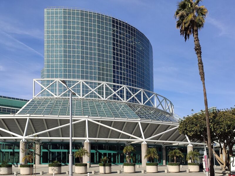 The glass tower entrance of the Los Angeles Convention Center with palm trees under a blue sky