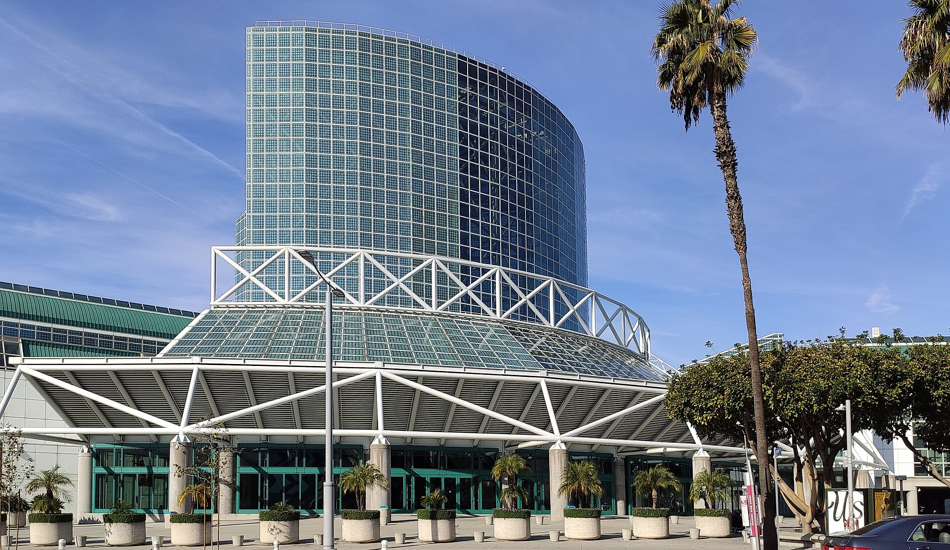 The glass tower entrance of the Los Angeles Convention Center with palm trees under a blue sky