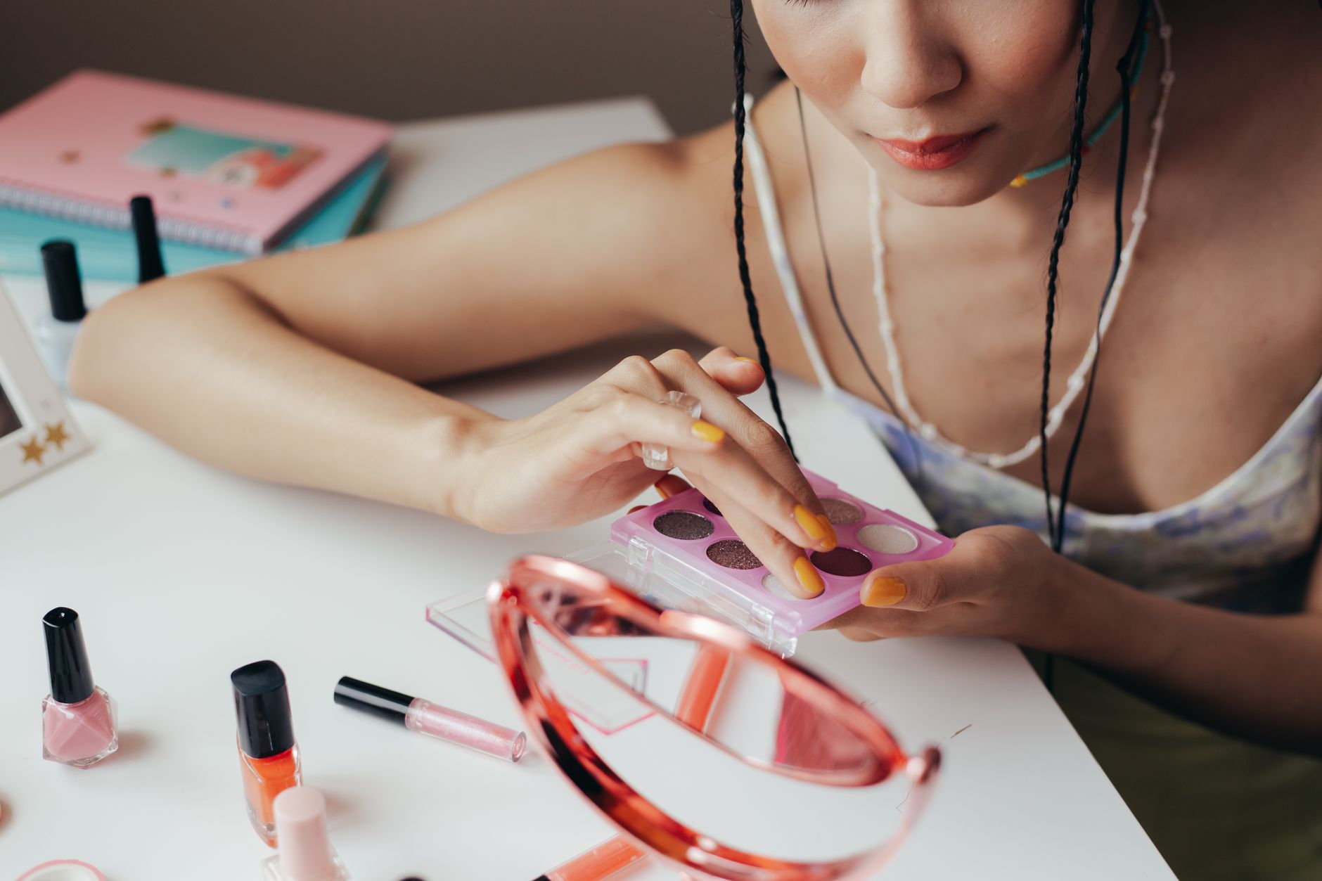 Person painting her nails at a table with makeup and a headband.