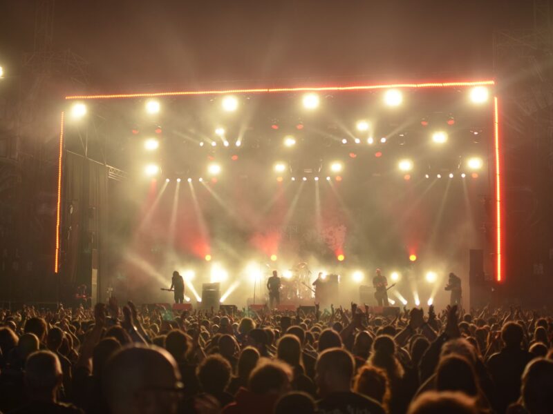 Concert crowd facing a brightly lit stage at night.