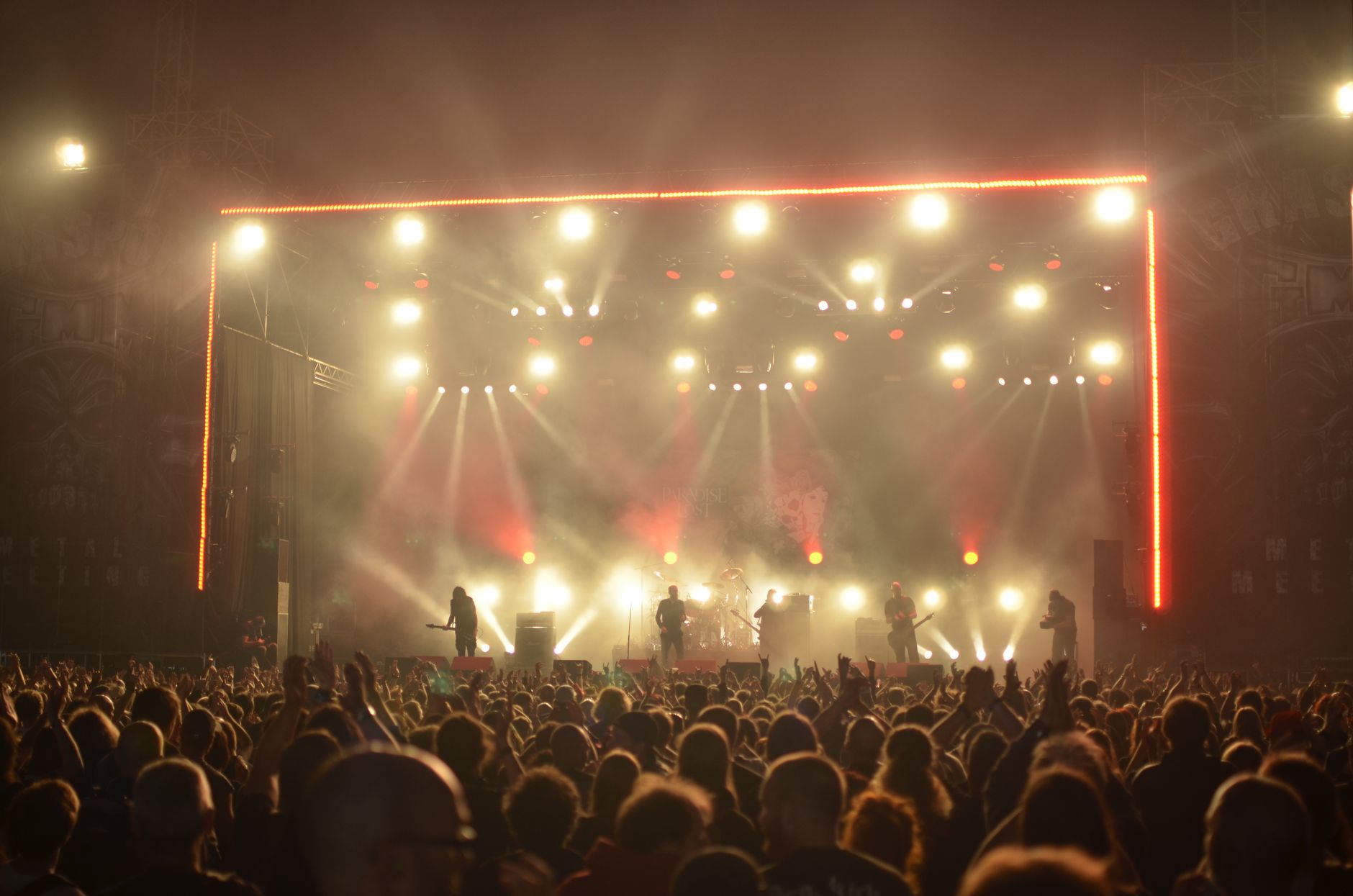 Concert crowd facing a brightly lit stage at night.