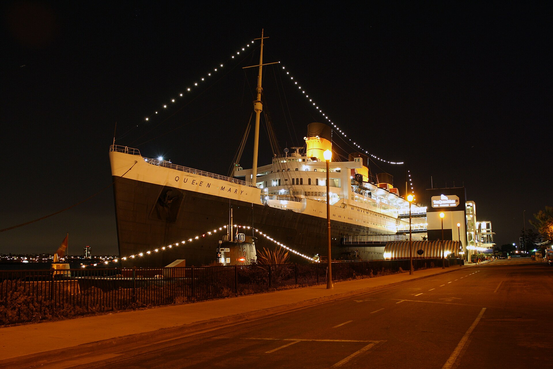 The Queen Mary ocean liner lit up with strings of lights at night along the Long Beach waterfront