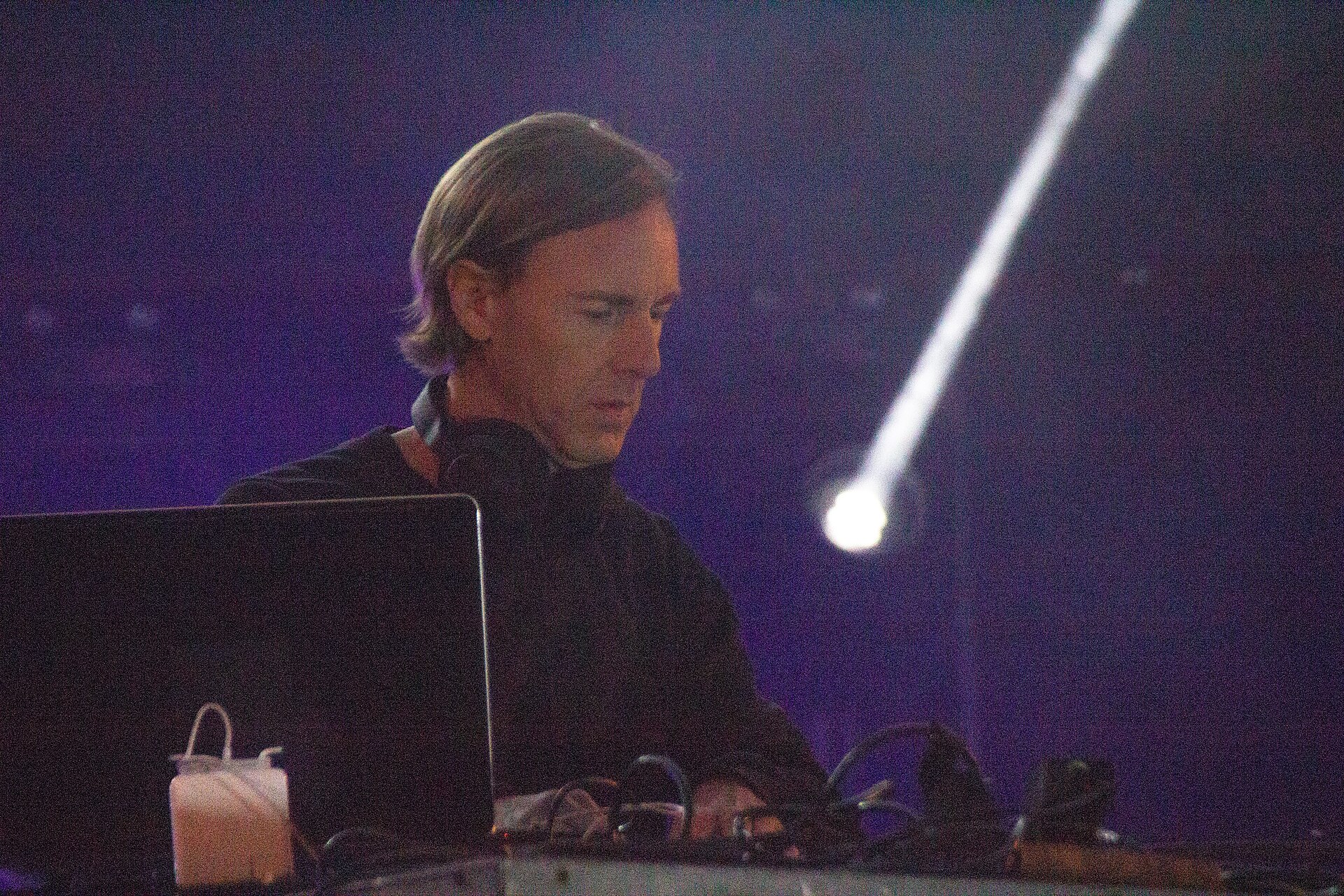 Richie Hawtin DJing under blue stage light with a white spotlight beam behind him