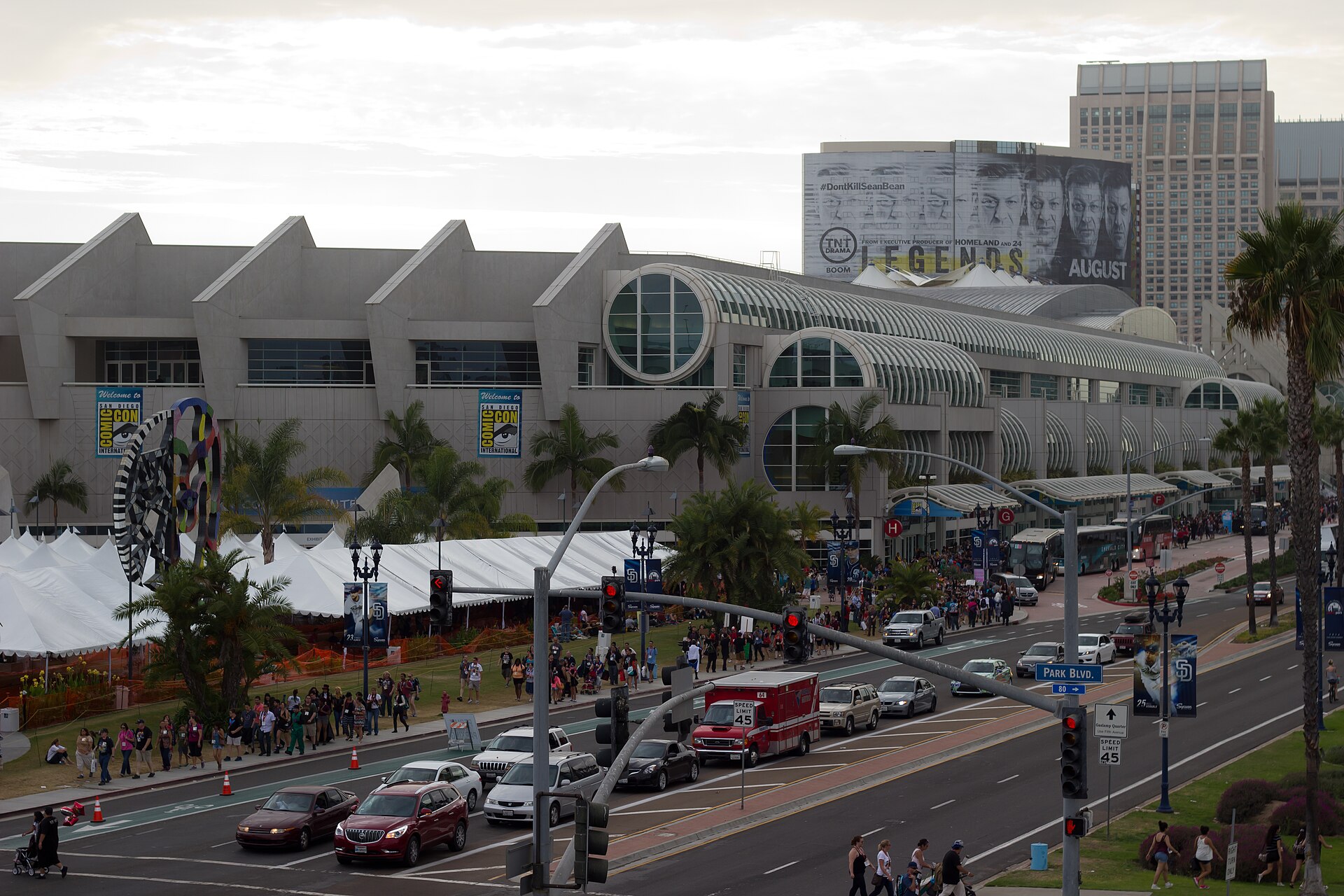 Crowds and white tents outside the San Diego Convention Center during Comic-Con week, with palm trees and traffic on the street in front