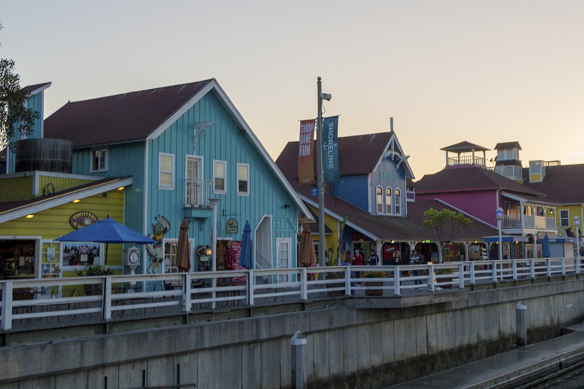 Colorful waterfront shops and a boardwalk railing at Shoreline Village in Long Beach at dusk