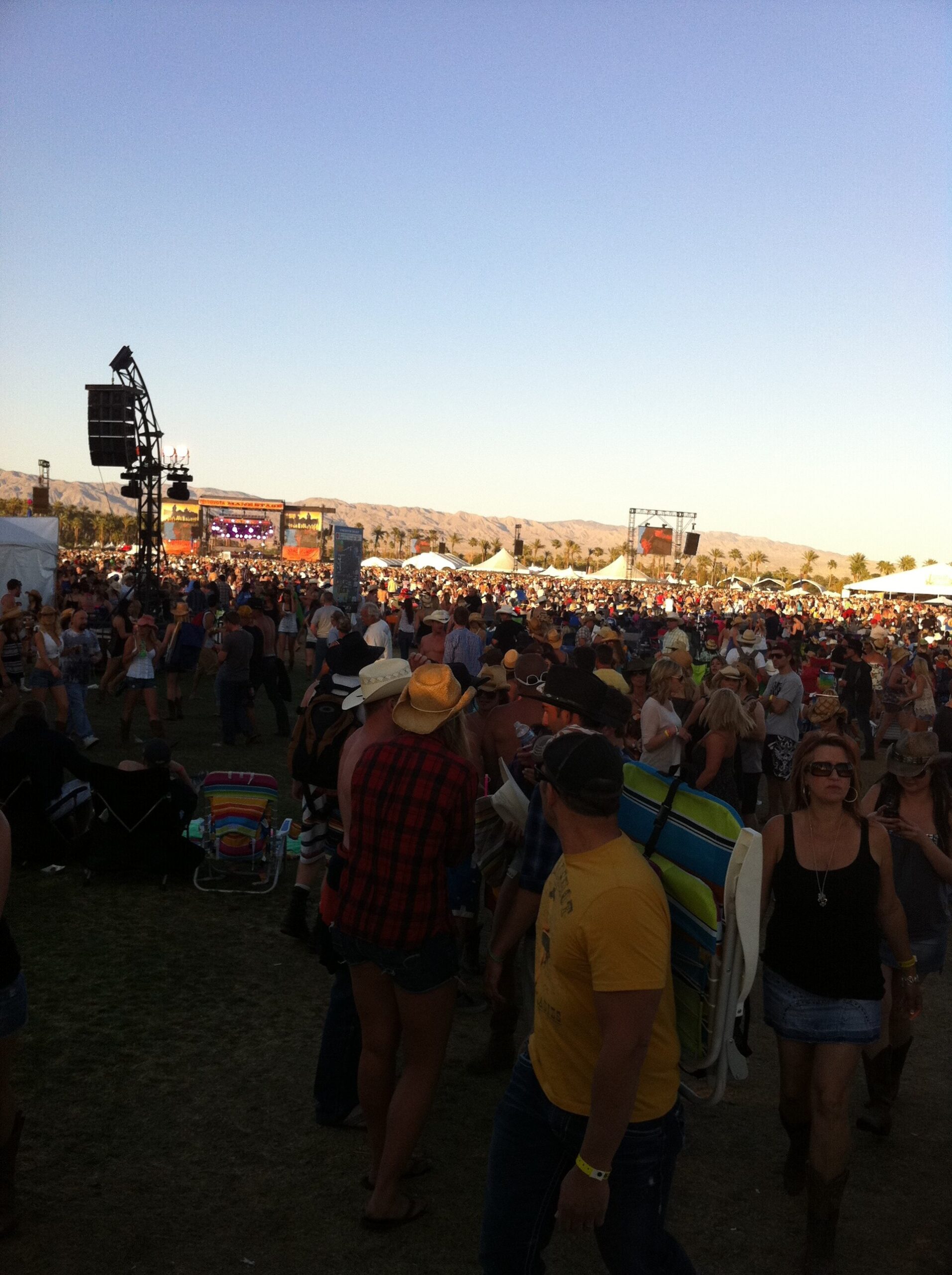 A crowd of festivalgoers at Stagecoach in Indio at dusk, with a tower silhouetted against a clear sky
