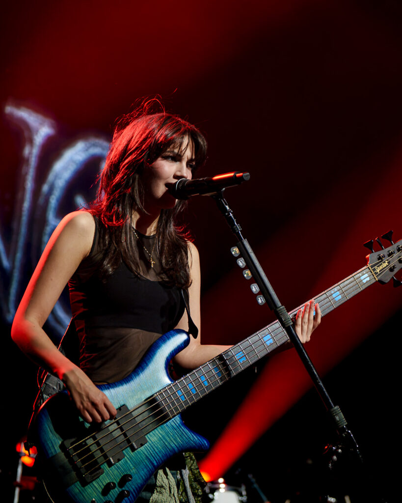 The-Warning-The-Fonda-Theater-Zharmaine-Boatman-The-824-Journal-33 – The 824 Journal The Warning at The Fonda Theatre in Los Angeles: female bassist singing into a microphone on stage, playing a blue electric bass under red lights.
