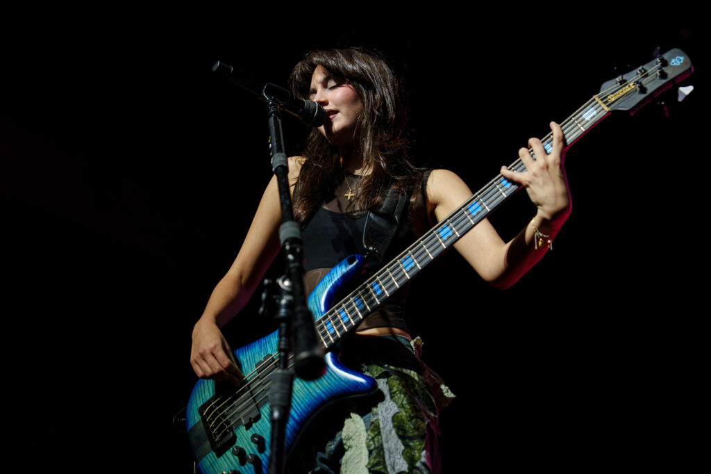 The-Warning-The-Fonda-Theater-Zharmaine-Boatman-The-824-Journal-5 – The 824 Journal The Warning at The Fonda Theatre in Los Angeles: female bassist singing into a microphone while playing a blue-green electric bass on stage.