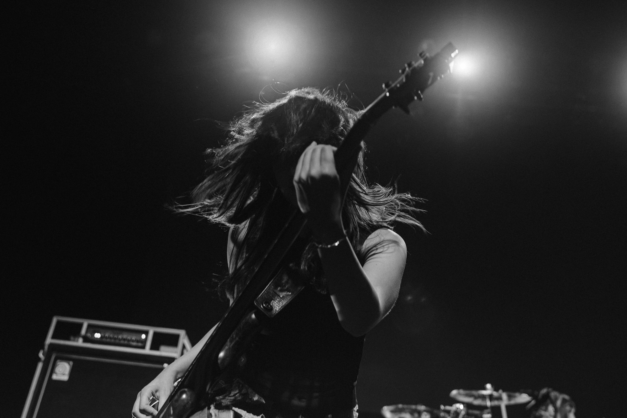 The-Warning-The-Fonda-Theater-Zharmaine-Boatman-The-824-Journal-7 – The 824 Journal The Warning at The Fonda Theatre in Los Angeles: guitarist on stage, backlit by bright lights, hair swinging as they play a guitar in a black-and-white concert shot.